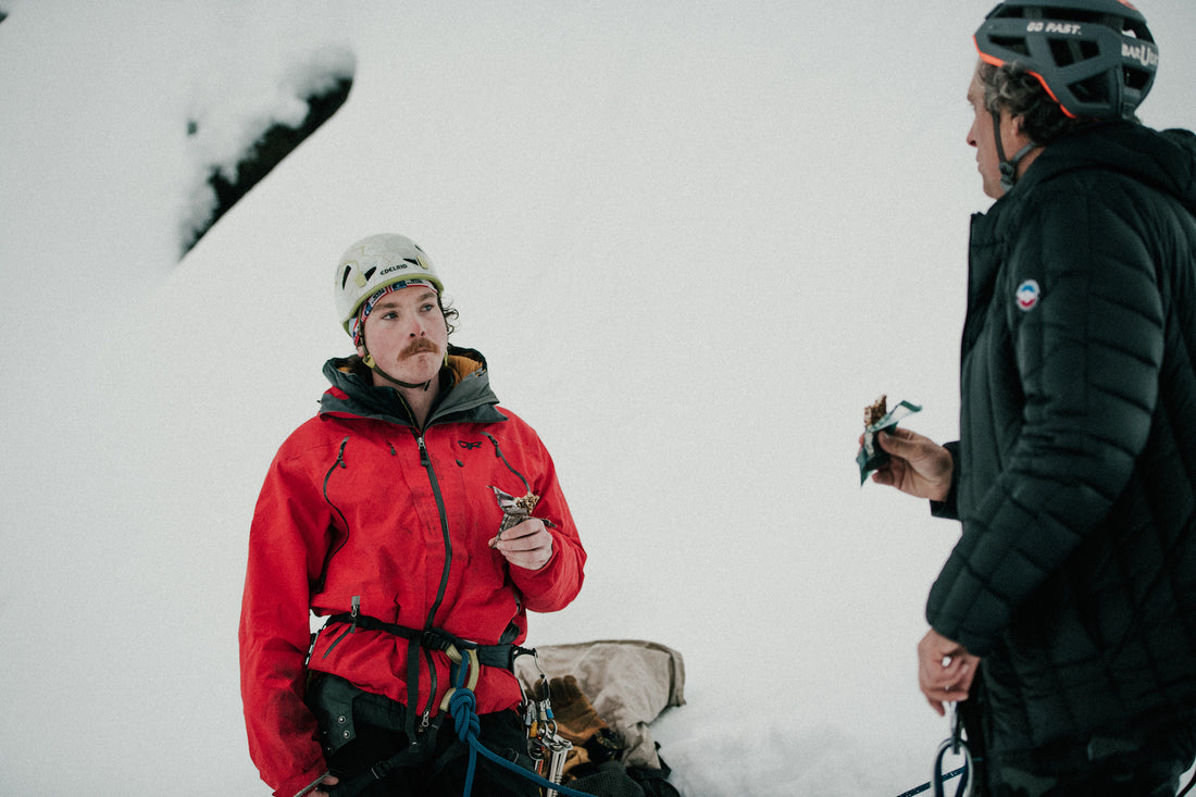 Two guys eating bars in the snow