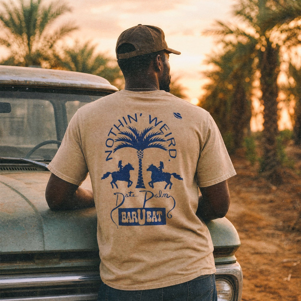 man leaning over the hood of a vintage truck with date palms in the background
