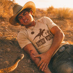 man laying on the ground wearing the rex riding shirt holding his arm that was just bitten by a snake