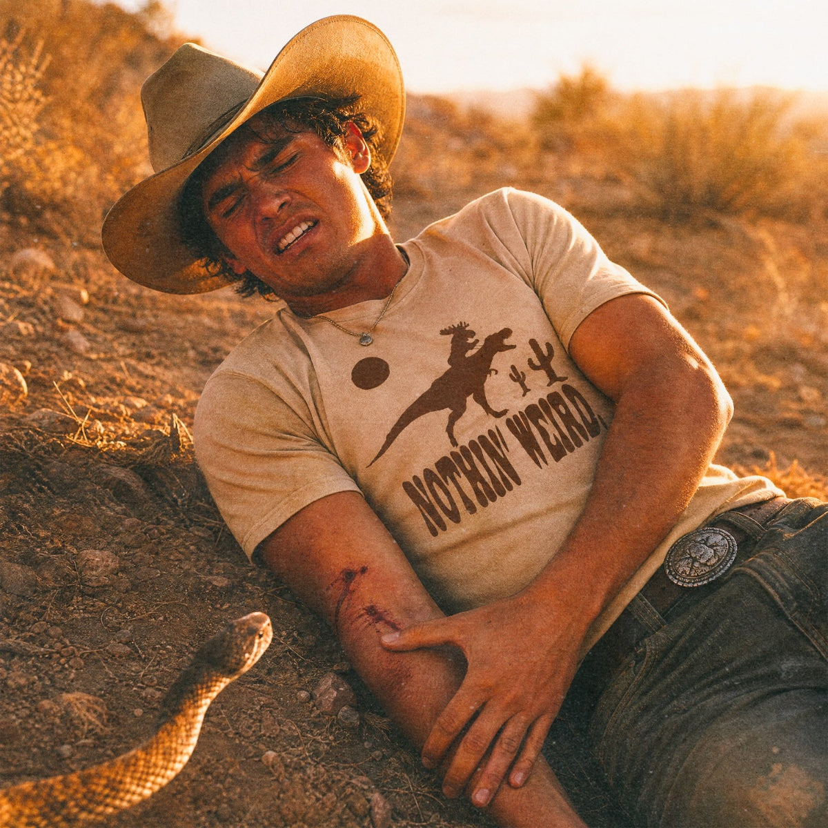 man laying on the ground wearing the rex riding shirt holding his arm that was just bitten by a snake