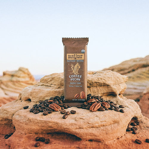 Barueat Coffee Pecan energy bar on a rock with coffee beans and pecans