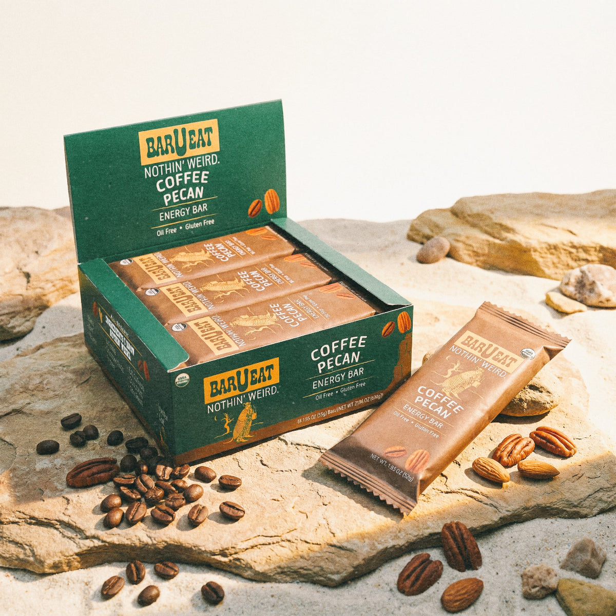 Box of Barueat Coffee Pecan energy bars on a rocky surface with coffee beans and pecans.