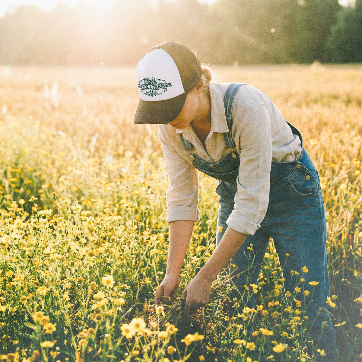 woman in a field harvesting plants wearing a granola farmer hat from barueat
