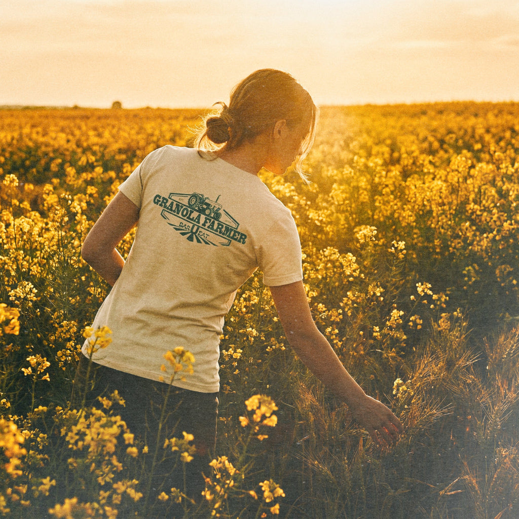 Person standing in a field of yellow flowers wearing a barueat 'Granola farmer' t-shirt.