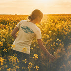 Person standing in a field of yellow flowers wearing a barueat 'Granola farmer' t-shirt.