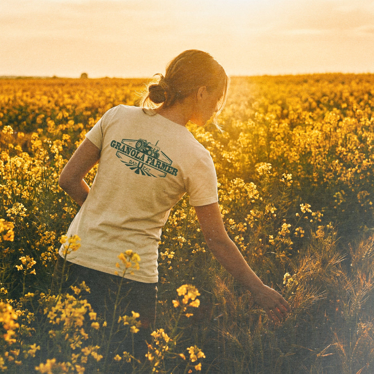 Person standing in a field of yellow flowers wearing a barueat 'Granola farmer' t-shirt.