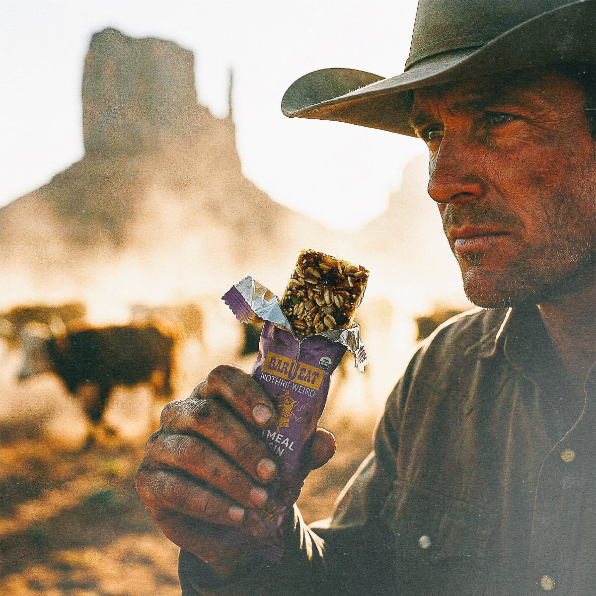 Man in cowboy hat holding a barueat oatmeal raisin bar with a desert landscape in the background