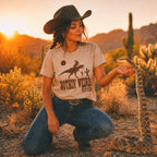 Woman in cowboy hat and 'Nothin' Weird' shirt interacting with a snake in a desert setting. 