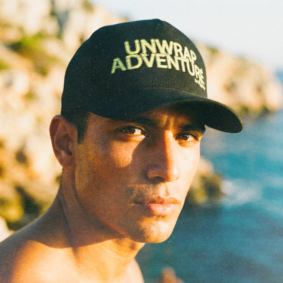 Man wearing the barueat unwrap adventure hat on the coastline with cliff behind him