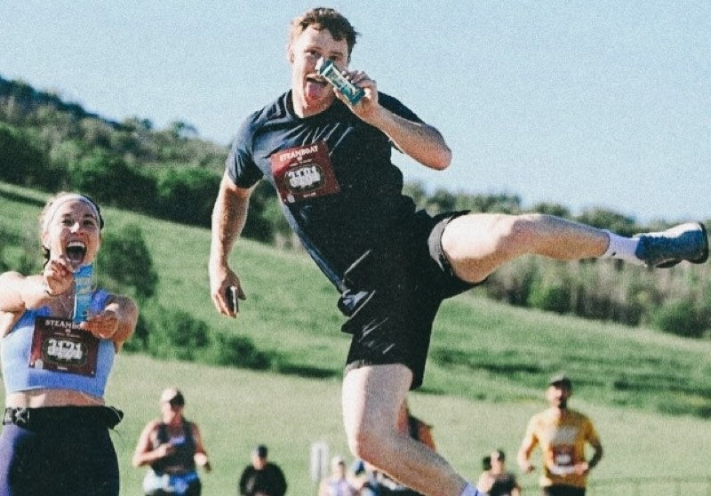 Two runners mid-race in Steamboat, one leaping through the air while eating a Bar U Eat bar
