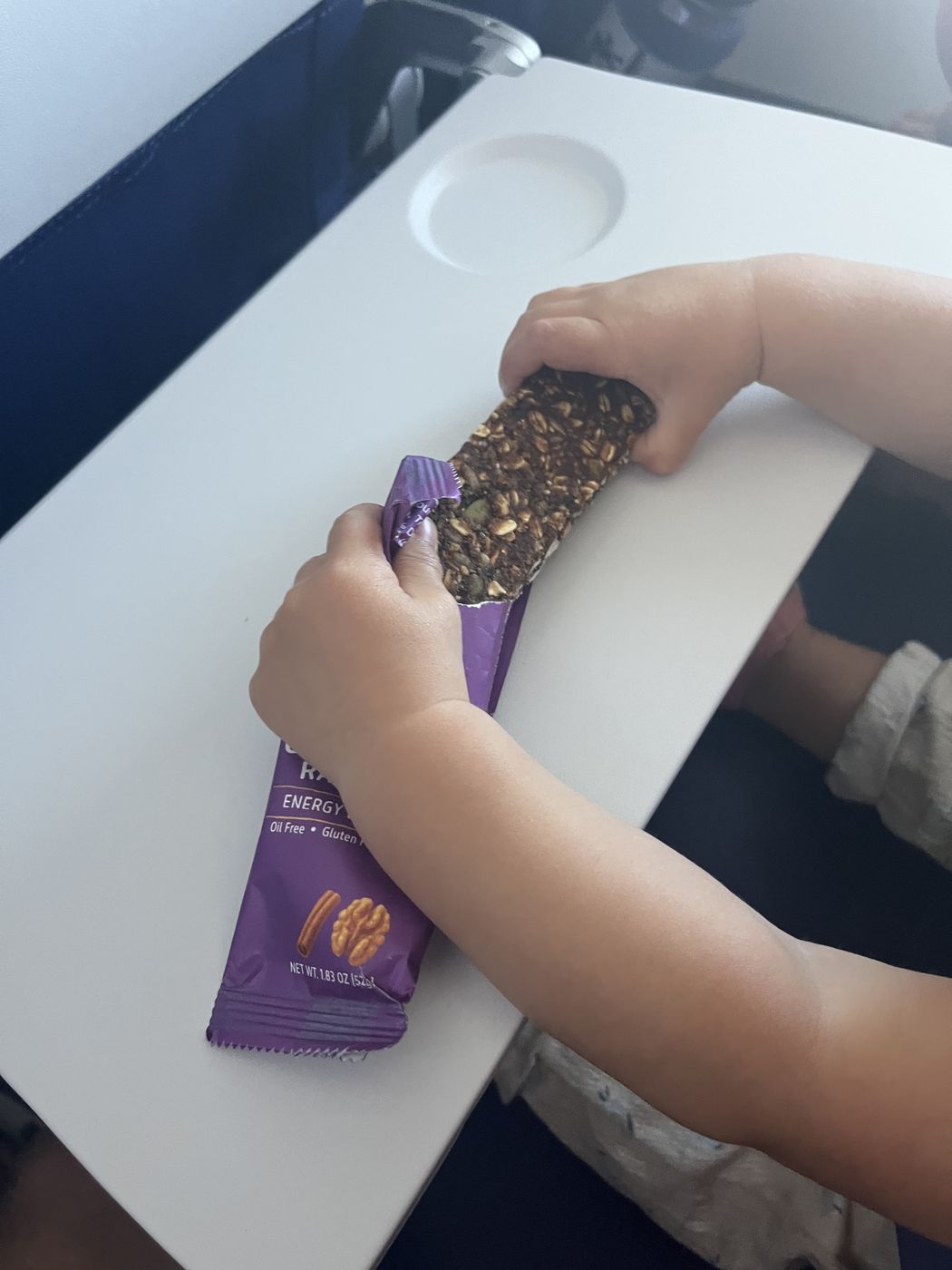 A young child's hands holding an unwrapped Bar U Eat bar over a white table