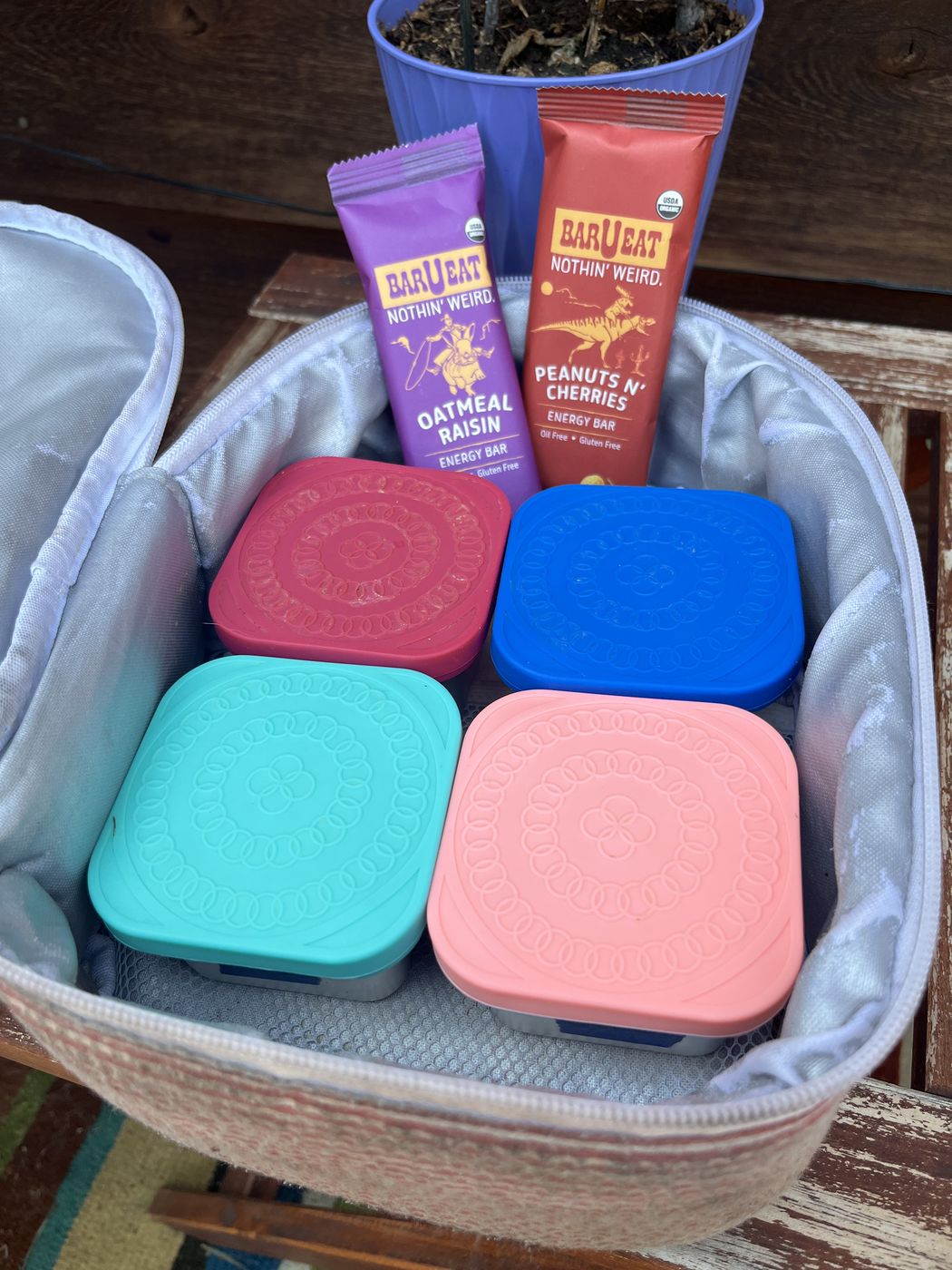 An open insulated bag packed with bento containers and Peanuts N' Cherries and Oatmeal Raisin bars